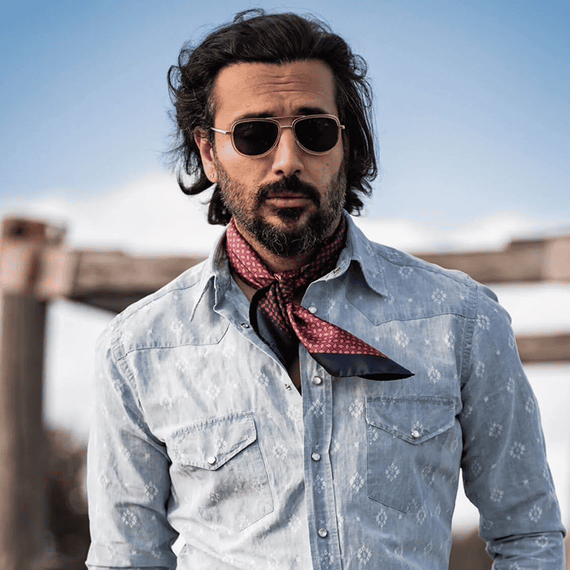 a men individual wearing a light blue floral-patterned denim shirt with a calm red neckerchief. a men individual wearing a light blue floral-patterned denim shirt with a calm red neckerchief.